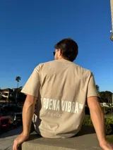 Remera de corte semi oversize en color beige, con estampado gráfico en la espalda que incluye la frase 'BUENA VIBRA' en letras grandes y 'feel the vibes' en tipografía cursiva, además de un pequeño logo bordado en la nuca.