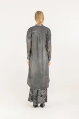Camisa larga de silueta amplia en color gris, con cuello mao y cierre frontal de botones. Presenta hombros caídos, mangas largas semitransparentes, cuatro bolsillos delanteros grandes, ruedo redondeado y pliegue central en la espalda.