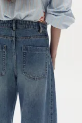 Pantalón de jean de pierna ancha y tiro alto, con bolsillos delanteros y traseros, presillas para cinturón y costuras verticales al frente.