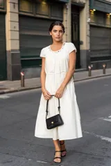 Vestido midi blanco de corte recto con escote redondeado y detalle de frunces. Tiene lazo en la cintura para ajustar la silueta y mangas cortas.