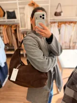 Cartera tipo hobo de diseño relajado, confeccionada en material con textura simil gamuza color chocolate. Presenta una silueta suave, cierre superior y asa corta combinada en simil cuero al tono.