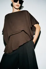 Top tipo capa blanco de punto fluido, con mezcla de viscosa, cuello bote, mangas cortas y bajo asimétrico.