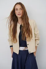 Chaqueta de corte recto y estilo minimalista en color beige, con cuello redondo, cierre frontal con botones y mangas largas con puños abotonados.
