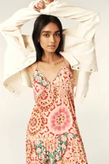 Vestido largo con estampado caleidoscópico en tonos rosa, rojo y verde. Presenta tirantes finos, escote en V, corte imperio y falda con volantes. Incluye detalle de trenzas en el pecho y la cintura que se anudan en la espalda descubierta.