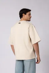 Remera de corte oversize color beige, con cuello redondo y etiqueta decorativa pequeña en el ruedo inferior.