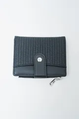 Billetera plegable color negro, con cierre a presión metálico en la solapa frontal. Presenta un panel superior con textura tejida y un panel inferior liso. Posee un bolsillo exterior con cierre metálico plateado en la parte inferior.