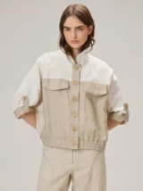 Chaquetas de lino bicolor en tonos blanco y beige, con diseño holgado, cuello alto, cierre frontal de botones, bolsillos con solapa en el pecho y mangas cortas con presilla y botón.