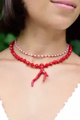 Collar doble compuesto por una gargantilla de cuentas pequeñas en tonos rojo y blanco, y un collar de cuentas facetadas rojas con un dije central en forma de rama de coral.