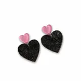 Aros colgantes con forma de corazón, uno pequeño rosa con glitter y otro grande negro con glitter.