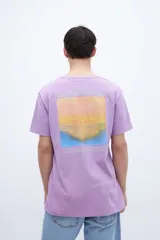 Remera lila de manga corta con estampa fotográfica en la espalda que muestra un paisaje de atardecer sobre el mar.