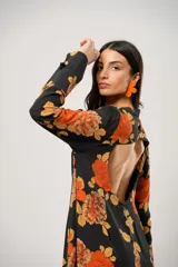 Vestido largo negro con estampado de flores naranjas y amarillas, cuello mao con abertura en forma de gota, mangas largas acampanadas con botones en los puños, tajo lateral y flecos en el ruedo.