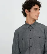 Camisa de manga larga gris con textura, cierre con botones, cuello clásico y bolsillo en el pecho.