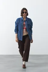 Sobrecamisa de jean azul con silueta relajada, cuello camisero, cierre frontal con botones metálicos y bolsillos utilitarios frontales.