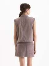 Chaleco de denim color marrón, con cuello camisero, cierre frontal con broches metálicos y bolsillos delanteros parcheados.