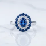 Anillo de plata 925 con diseño ovalado, presenta una piedra central en color zafiro rodeada por un doble halo de circonias blancas y azules.