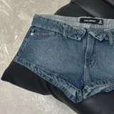 Short de denim azul de tiro bajo, con diseño clásico de cinco bolsillos, trabillas para cinto y cierre frontal con botón y cremallera.