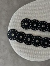 Cinturón de ecocuero negro con diseño de círculos unidos, cada uno con un ojal central grande y múltiples ojales pequeños alrededor.