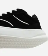 Championes de estilo skater para hombre, confeccionados en poliuretano color marrón oscuro. Poseen punta redonda, caña baja y suela de plataforma blanca. Destacan por sus cordones anchos tipo fat lace y detalles laterales en contraste.