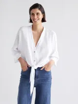 Camisa blanca de lino con escote en V, mangas largas y cierre frontal con botones. Se ata en la parte inferior con un lazo.