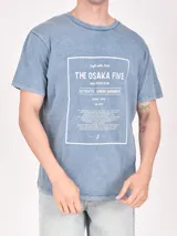 Remera color beige con estampa rectangular con diseño abstracto en tonos marrones y texto.