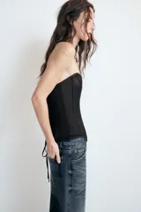 Top corsetero semitransparente con escote palabra de honor, detalle de varillas interiores y bajo asimétrico. Cuenta con cierre lateral con cremallera oculta.