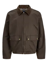 Campera de estilo worker color marrón, con cuello camisero de pana, cierre frontal con cremallera y bolsillos frontales con solapa y broches a presión. Presenta un acabado recubierto que le otorga una textura sutilmente brillante y resistente.