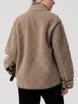 Campera polar de textura suave con diseño acolchado de rombos, cuello alto y cierre frontal con botones. Presenta ribetes en contraste, bolsillos frontales amplios y mangas largas.