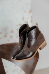 Botinetas de caña baja combinadas en cuero con textura de cocodrilo y gamuza en color marrón oscuro. Presentan un diseño de estilo western con taco bajo de madera y cierre lateral.