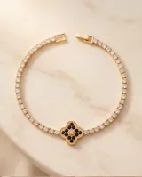 Pulsera de acero con baño dorado, compuesta por una cadena de circonias cúbicas y un dije central en forma de trébol decorado con circonias negras y blancas.