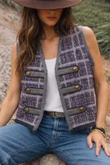 Chaleco sin mangas de tejido de punto con diseño a cuadros en tonos violeta y gris. Presenta un estilo militar con detalles de tiras horizontales en cuero sintético gris y botones dorados decorativos en el frente.