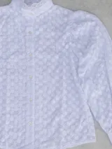 Blusa blanca con cuello alto con volados, mangas largas abullonadas y estampado floral en relieve.