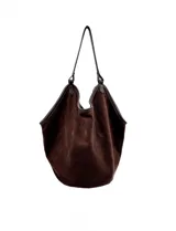 Cartera tipo hobo de gran capacidad confeccionada en símil gamuza color marrón. Presenta un diseño relajado y flexible con base reforzada y ribetes de cuerina a juego. Cuenta con una sola asa de hombro integrada a la estructura y un compartimento interior independiente.