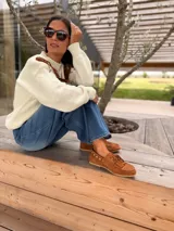 Náuticos de gamuza color suela con flecos en la parte delantera y detalle de tachas metálicas circulares en el lateral. Diseño artesanal con cordones frontales y suela plana.