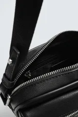 Bandolera negra con textura grabada, compartimento principal con cierre de cremallera, bolsillo interior con cremallera, bolsillo frontal con cremallera y asa de hombro ajustable.