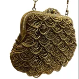 Bolso de mano estilo vintage, completamente bordado con mostacillas en tono dorado formando un patrón de escamas. Cuenta con una boquilla metálica dorada con cierre a presión y una cadena metálica a tono para llevar al hombro.