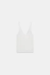 Top de punto canalé en color beige, con escote en pico adornado con una delicada aplicación de encaje blanco y tirantes anchos.