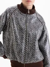 Campera tipo bomber con cierre frontal, cuello alto, puños y ruedo en tejido acanalado color marrón. Presenta un diseño estampado con patrón de espiga en tonos blanco y negro.