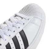 Championes Adidas Superstar de diseño clásico, con capellada de cuero blanco, icónica puntera de goma tipo Shell Toe y las tres bandas laterales en color negro. Presenta detalle en negro en el talón con el logo de la marca.