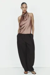 Pantalón negro de tiro alto, corte amplio estilo balloon o culotte, con pliegues marcados en el delantero y bolsillos laterales ocultos.