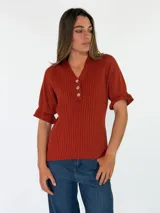 Top de tejido de punto color terracota, con escote en V, cuello camisero y cartera frontal con botones. Presenta mangas cortas con textura calada y puños con volados.