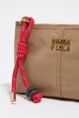 Monedero de nailon color tostado con cierre superior, tirador de cordón rojo trenzado con detalles de cuentas oscuras y terminales metálicas doradas, y logotipo metálico dorado de la marca en el frente.