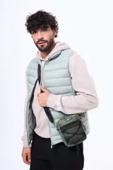 Morral de estilo urbano color verde militar, con compartimento principal con cierre, bolsillo frontal de malla con cordón elástico ajustable y correa de hombro regulable.