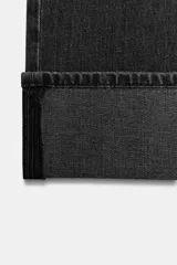 Jeans rectos de tiro medio en denim negro con efecto lavado. Presenta diseño de cinco bolsillos, trabillas para cinto y bajo con vuelta marcada. Cierre frontal con botones metálicos ocultos.