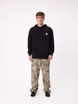 Canguro negro con capucha y cordones ajustables, con estampado gráfico en la espalda que incluye el logo de Rusty, texto "FIND YOUR SHELTER" y "ESCAPE THE NOISE", coordenadas geográficas y dibujos de plantas y árboles.