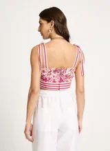 Crop top con estampado floral en tonos fucsia y blanco, breteles finos con lazos en los hombros y detalle de franjas horizontales en el bajo.