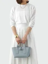 Cartera tipo tote de tamaño pequeño, confeccionada en cuero granulado color celeste. Presenta un diseño estructurado con asas cortas, cierre de solapa con el icónico broche de bambú metálico y correa ajustable para llevar cruzada.