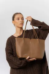 Cartera tipo tote de diseño amplio y estructurado, confeccionada en material sintético con textura graneada. Cuenta con doble asa larga para llevar al hombro y logo de la marca aplicado en el frente.