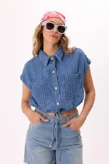 Camisa crop de denim texturado color celeste, con cuello camisero, mangas cortas, dos bolsillos frontales y lazo regulable en el ruedo.