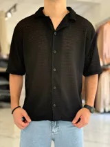 Camisa de manga corta negra con tejido texturizado tipo red, cuello camisero y cierre frontal con botones.