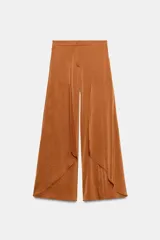 Pantalón fluido de tiro alto en color tostado, con pernera ancha y volantes superpuestos en la parte delantera. Cuenta con cierre frontal con cremallera, botón interior y gancho.